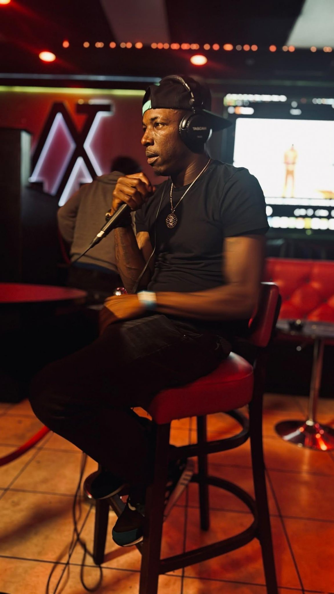 Twan G Young Gutta seated in a venue holding a microphone