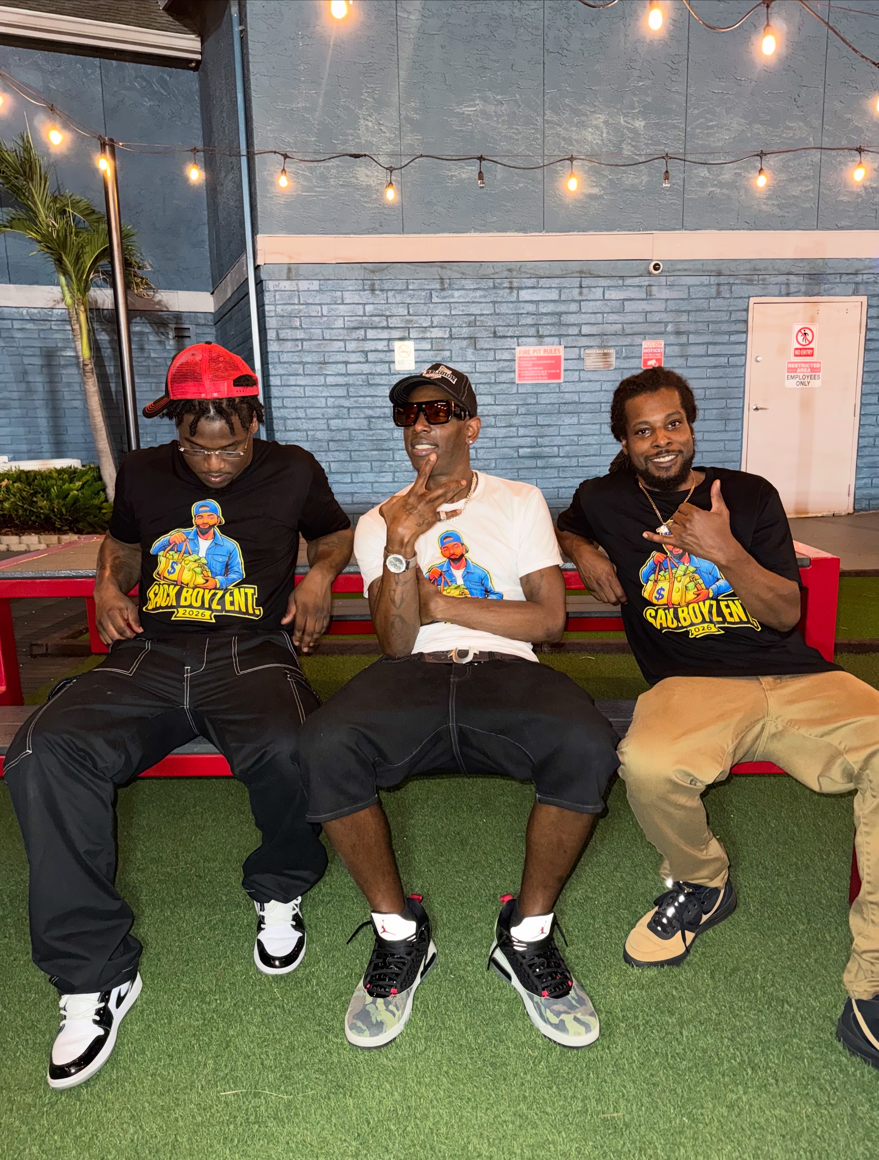 Chevy GC and two men wearing Sack Boyz Entertainment 2026 T-shirts while seated on a bench