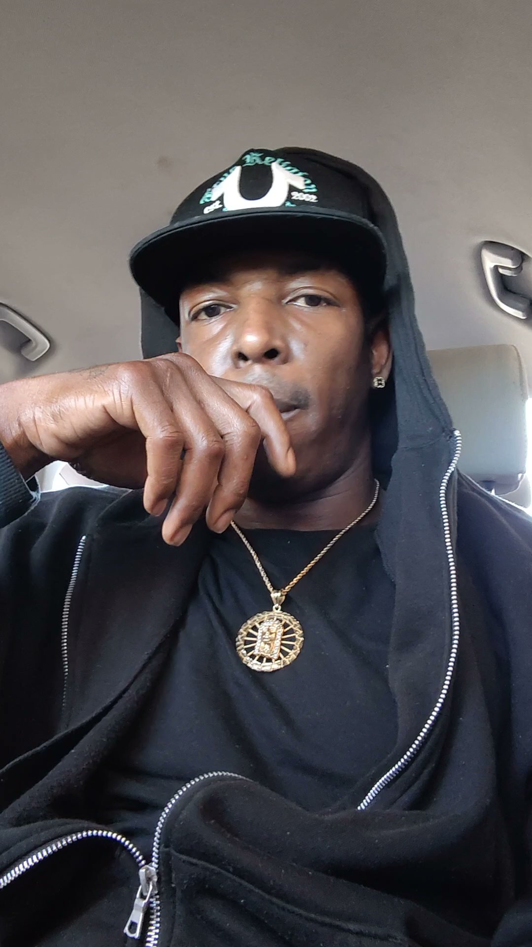 Close portrait of Twan G Young Gutta wearing a black True Religion cap inside a car