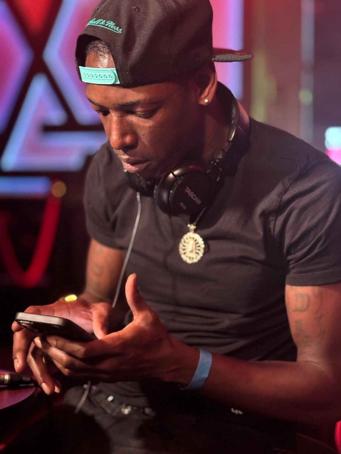Close portrait of Twan G Young Gutta checking his phone with headphones around his neck