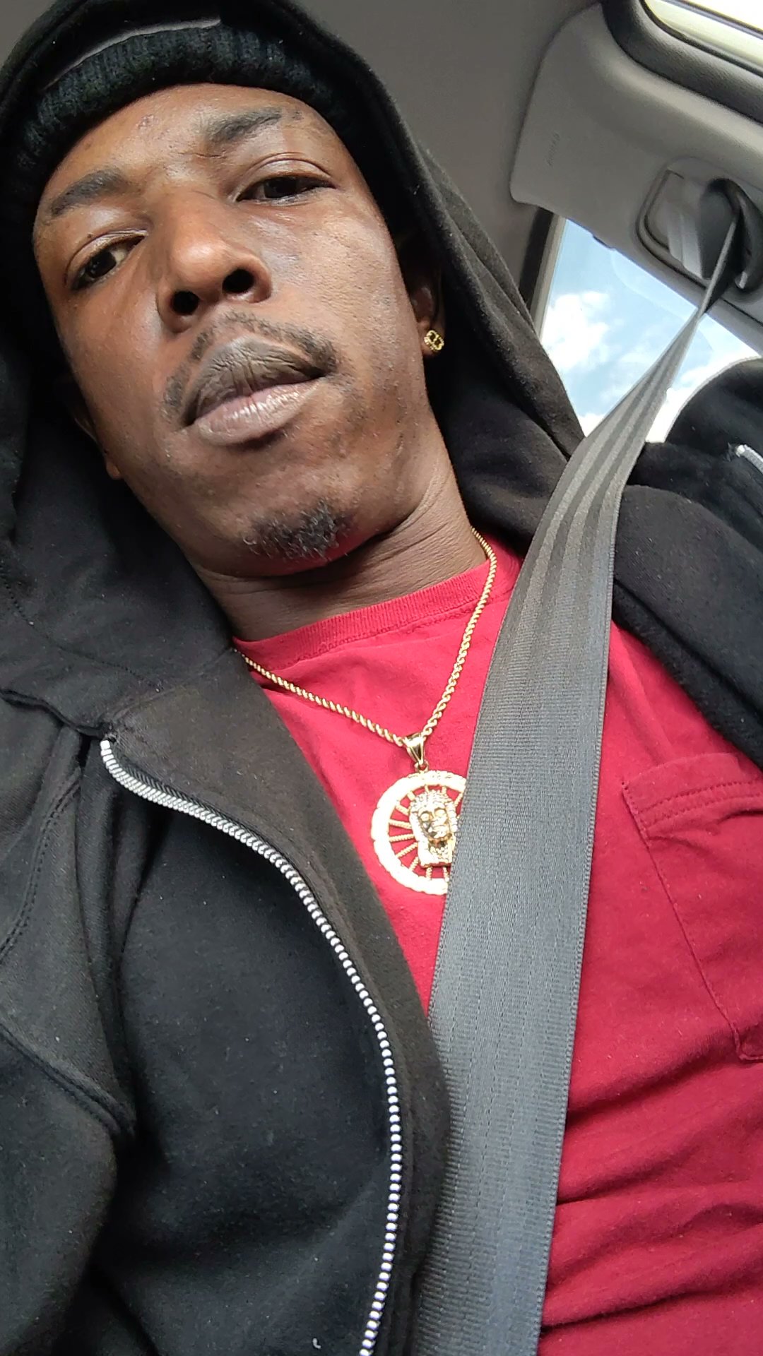 Close portrait of Twan G Young Gutta in a red shirt and black hoodie while seated in a car
