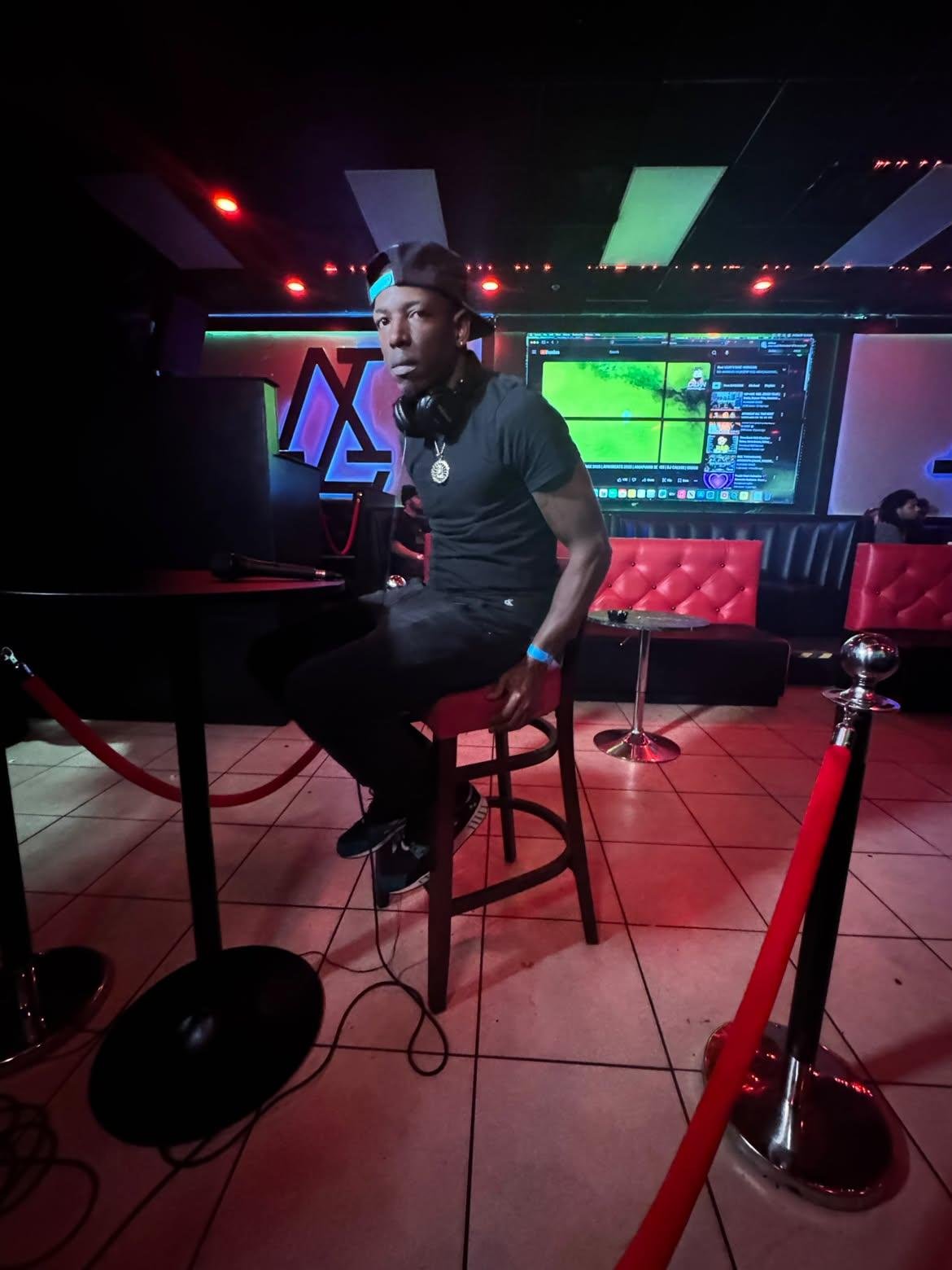 Twan G Young Gutta seated inside a red-lit venue with headphones around his neck